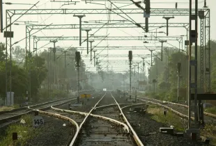 Railway tracks converging beneath overhead lines and signal gantries.