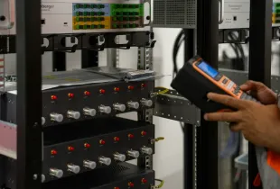 A technician inspecting network equipment racks with a handheld diagnostic tool.
