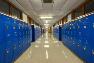 An empty school corridor lined on both sides with blue student lockers.