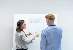 Two colleagues at a whiteboard working through a process framework diagram.