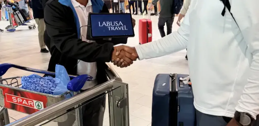 LT representative shakes hands with LABUSA Travel rep holding a tablet at Cape Town International Airport arrivals hall.