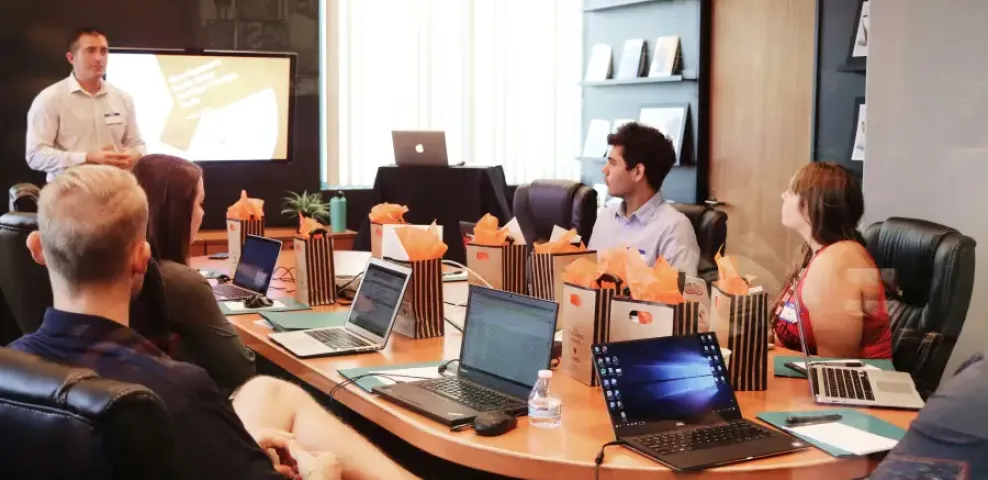 IT professionals attending a boardroom presentation with laptops and gift bags on a conference table.