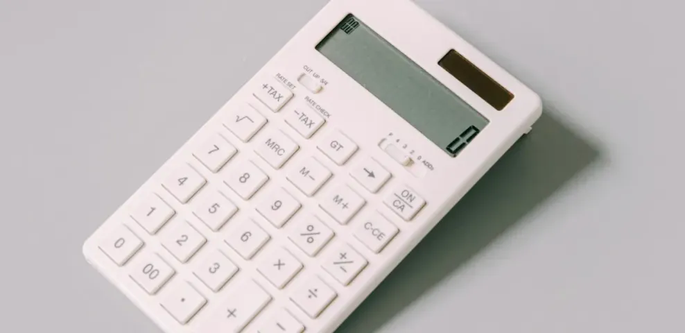 A plain white desk calculator lying on a light gray surface.
