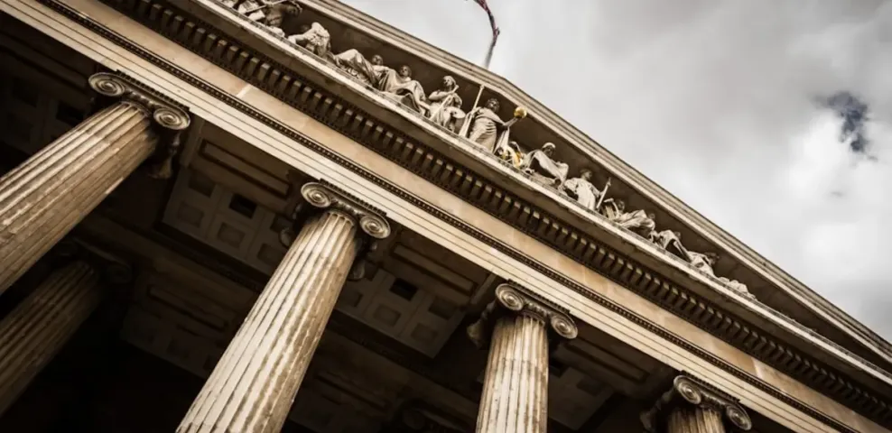 The stone columns and carved pediment of a classical civic building seen from below.