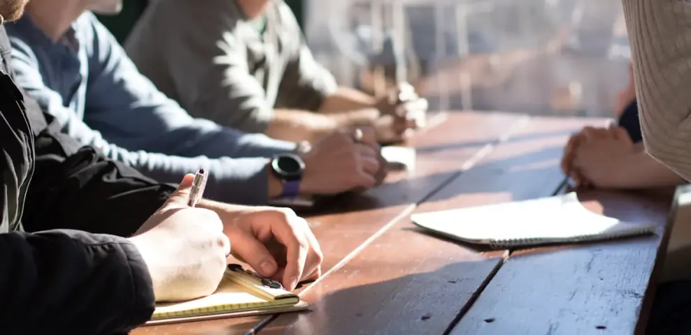 Four colleagues seated along a wooden table, writing notes during a working session.