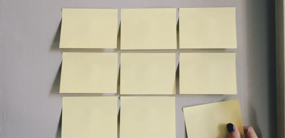 A hand placing a paper note into an ordered grid of notes on a wall.