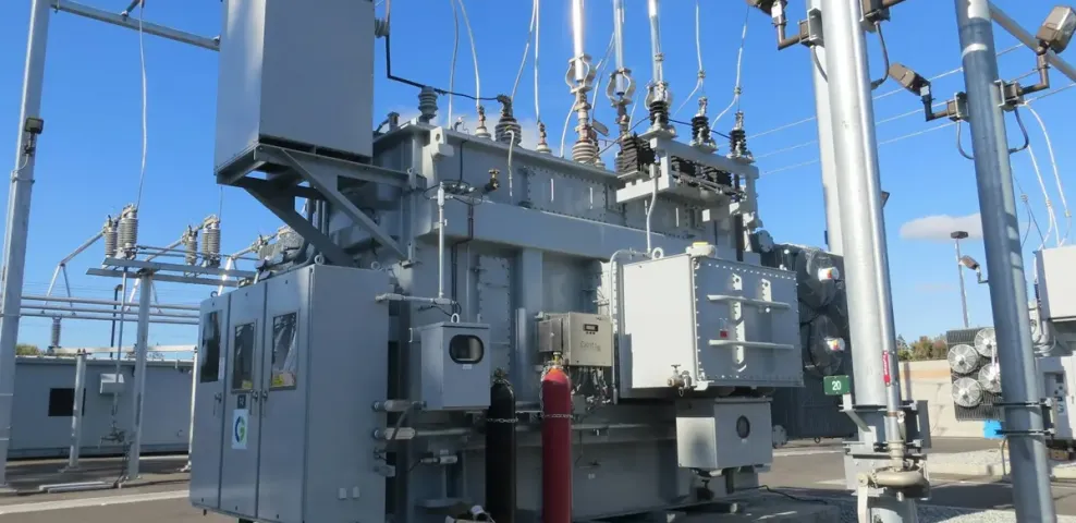 Transformer and switchgear equipment in an electrical substation under a clear blue sky.