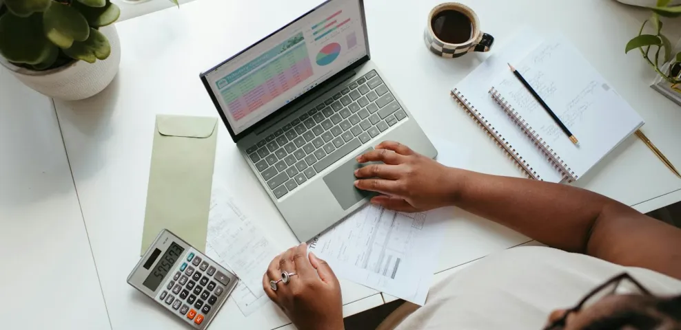 An overhead view of a desk with a laptop showing a budget spreadsheet, a calculator, and a notebook.