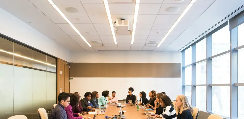 People meeting around a long boardroom table with laptops and papers.