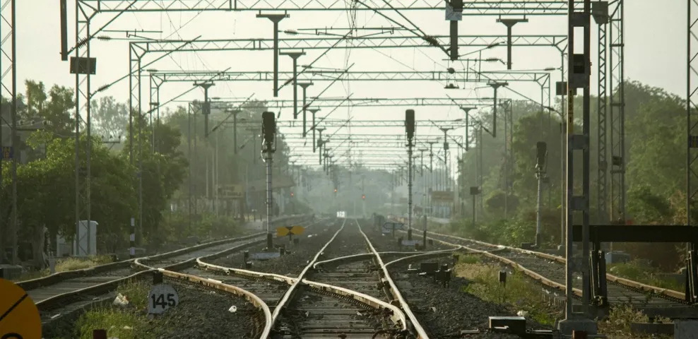 Railway tracks converging beneath overhead lines and signal gantries.
