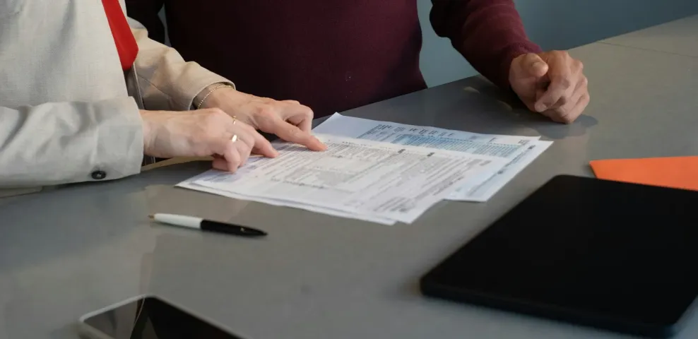 Two colleagues reviewing a printed form together at a desk with a pen.